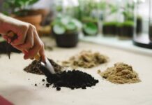 Close-up of a hand using a small shovel to sort different soil types on a table.