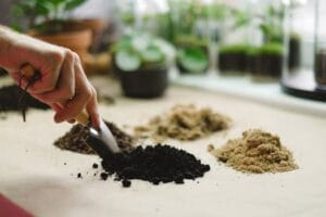 Close-up of a hand using a small shovel to sort different soil types on a table.
